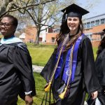 two students and a faculty member in academic regalia walk across campus