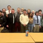 a group of students faces the camera, standing behind a table