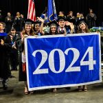 A group of students in caps and gowns carry the class of 2024 banner at commencement