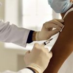 a doctor in a white coat administers a vaccine in the arm of a patient