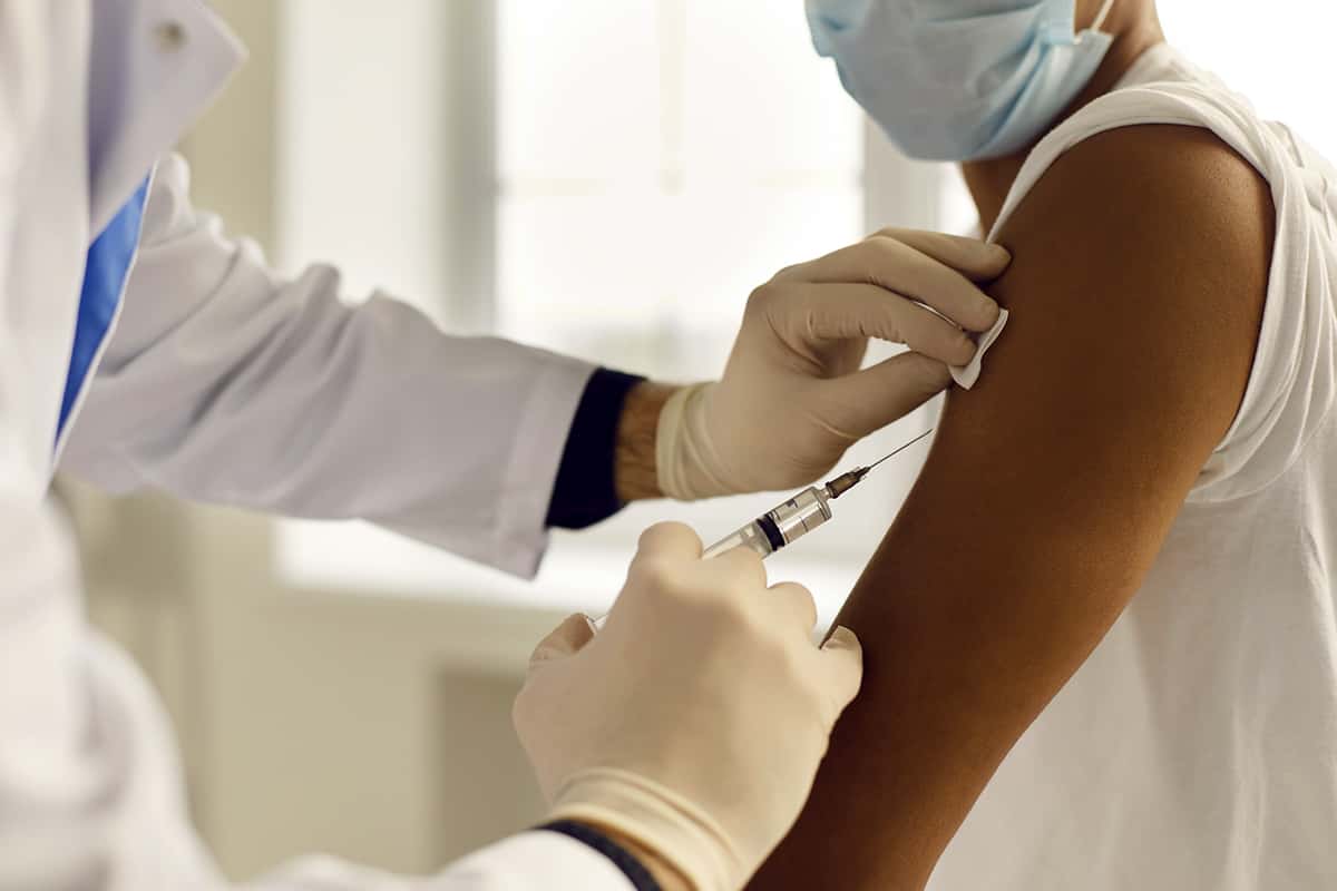 a doctor in a white coat administers a vaccine in the arm of a patient
