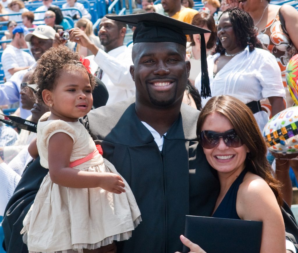 Wearing a graduation cap and gown, Cesaire poses with his wife and daughter after participating in the 2011 commencement ceremony.