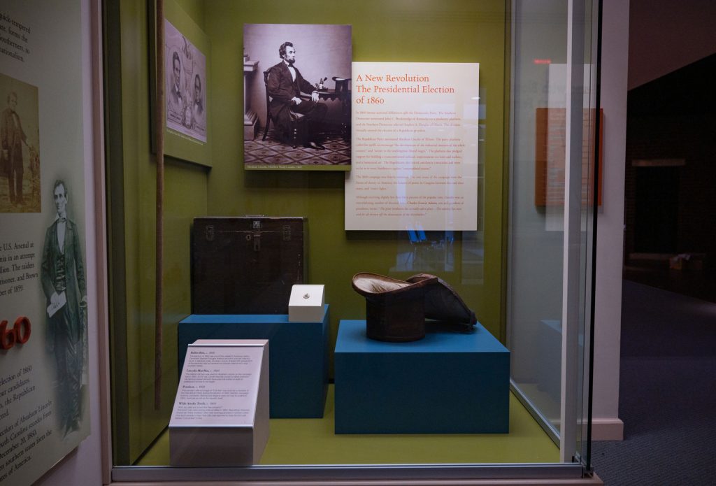 An exhibit on the “Presidential Election of 1860” includes Abraham Lincoln’s hatbox, a ballot box, and a pendant with an image of “Old Abe” worn by a member of the Republican Party. 