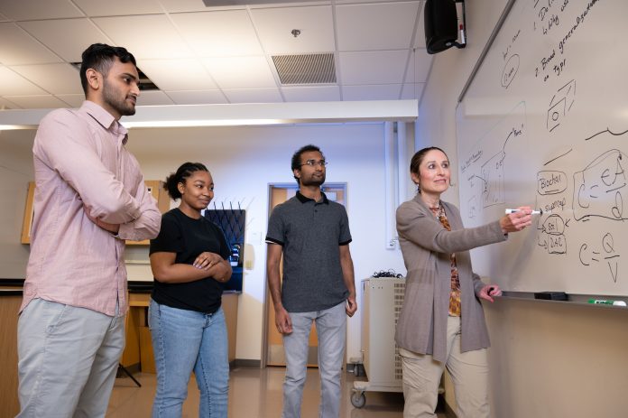 Students standing around whiteboard with professor giving instruction