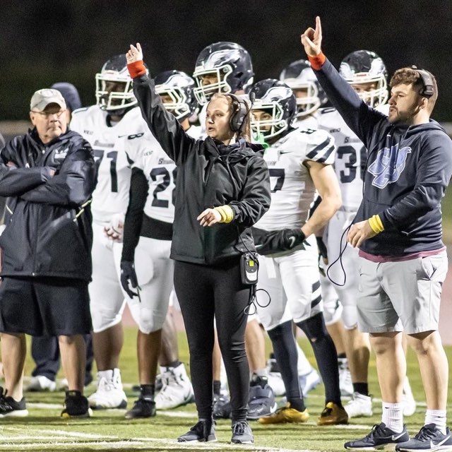 With members of the Owls football team lined up behind her, sophomore Charliana Criscuolo rises her hand to direct players on the field during a game.