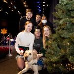 Students posing with dog besides Christmas Tree.