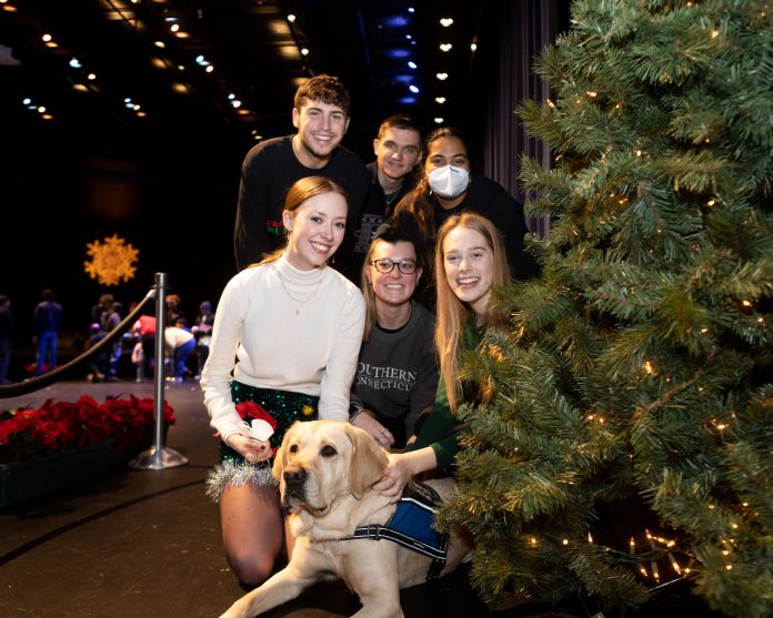 Students posing with dog besides Christmas Tree.