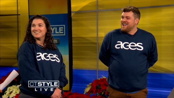Two adults with ACES shirts in a television studio smiling to the left.