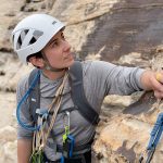 Woman with climbing gear stands in front of ledge