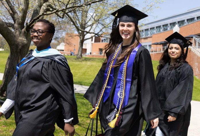 two students and a faculty member in academic regalia walk across campus