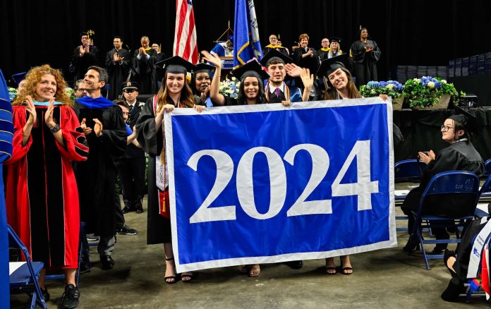 A group of students in caps and gowns carry the class of 2024 banner at commencement