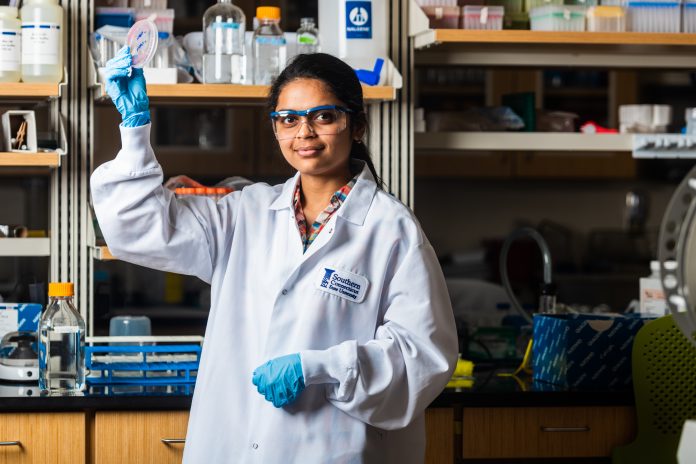 a student in a white lab coat stands in a chemistry lab