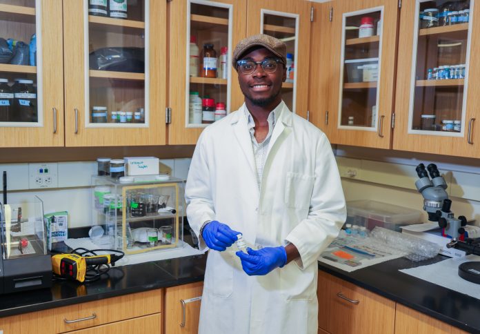 a student in a white lab coat stands in a lab