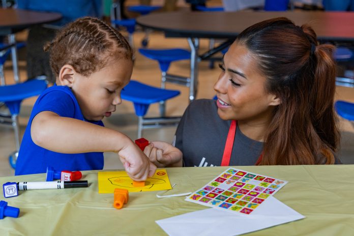 a young child and a preschool teacher work together on a small art project