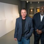 two educators standing next to a large, white artwork.