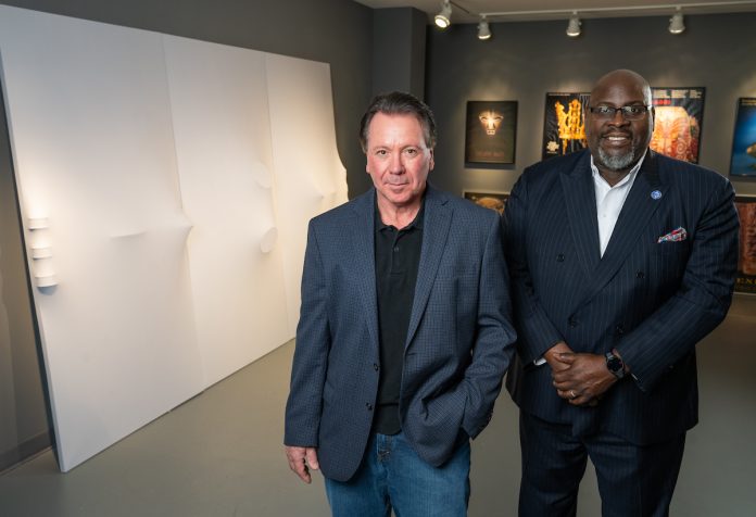 two educators standing next to a large, white artwork.