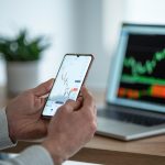 person looking a phone and stock market ticker
