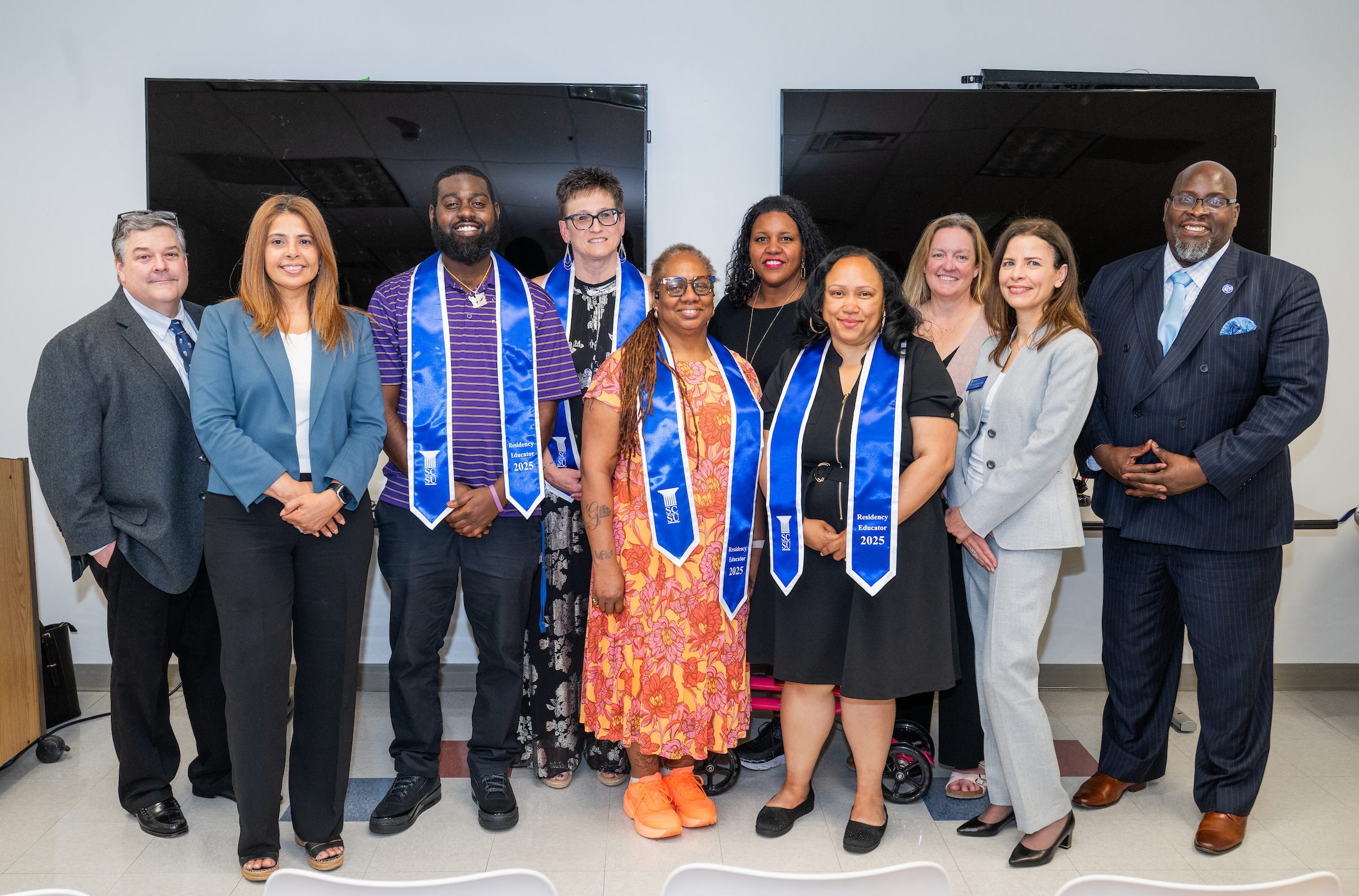 A group of 4 graduates wearing stoles pose with program administrators at a celebration event.