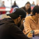 a student sits at a table, looking at his phone