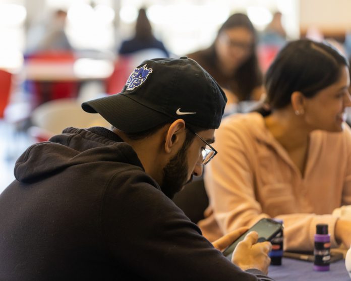 a student sits at a table, looking at his phone