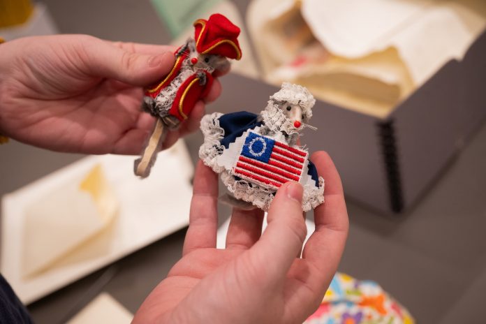 Close-up of two small mouselike handmade figurines dressed in colonial-era clothing and American flag patterns.