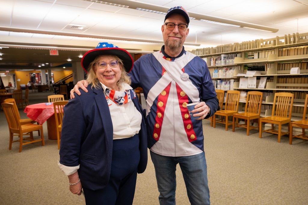A man and wome dressed in patriotic red, white, and blue clothing stand in the library