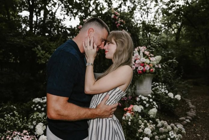 Taylor Swift and Travis Kelce embrace in a flower-filled garden following their engagement. The couple stands face-to-face, smiling as they hold each other among arrangements of pink and white blooms.