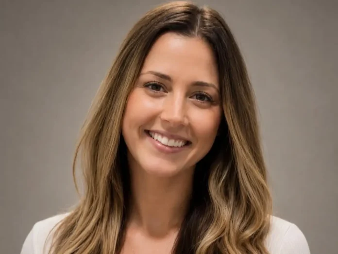 Headshot of Catherine DiGioia smiling at the camera against a neutral gray background. She has long brown hair with lighter highlights and is wearing a light-colored blazer.