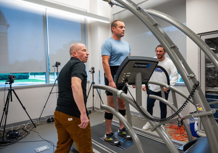 Robert Gregory, left, observes a participant walking on a treadmill in a Southern Connecticut State University health and movement sciences lab as another individual looks on.